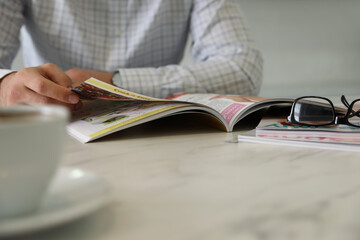 Man reading magazine at white table, closeup