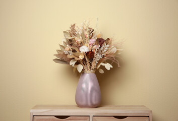 Beautiful dried flower bouquet in ceramic vase on wooden table near beige wall