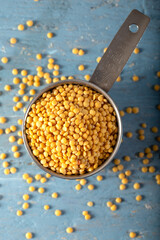 Yellow lentils in metal measuring cup on blue wooden background.