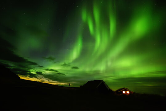 Night photo. Northern lights and a small house in the land overgrown with grass. Iceland.
