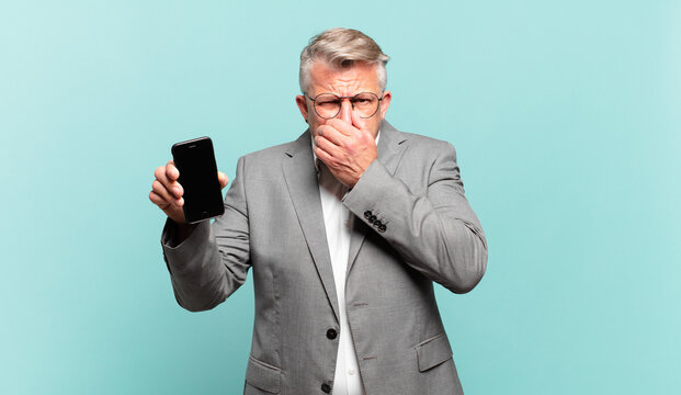 senior businessman covering mouth with hands with a shocked, surprised expression, keeping a secret or saying oops