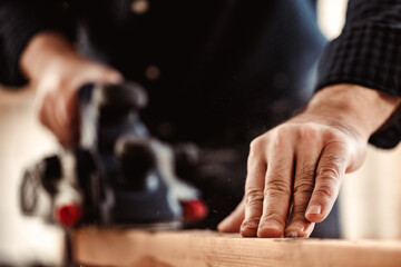 Carpenter's hands working with electric planer in a workshop