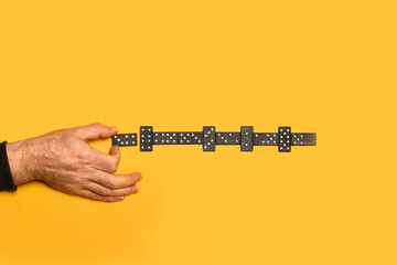 Mano de hombre sosteniendo una ficha de dominó sobre un fondo amarillo liso y aislado. Vista superior. Copy space