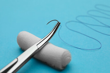 Forceps with suture thread and bandage roll on light blue background, closeup. Medical equipment