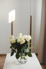  glass vase with white roses on white table indoors
