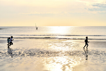 Fototapeta na wymiar 材木座海岸砂浜を走る子供たちと沖に浮かぶウインドサーフィン