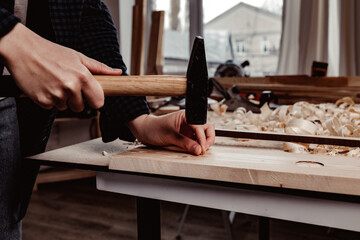 Human hands hammer nail into a wooden bar