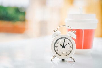 white analog clock at ten o'clock and blurred plastic hot coffee cup on desk for coffee break with...