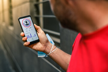 Close up of male hands using fitness app on smartphone. Man resting after jogging reading run...