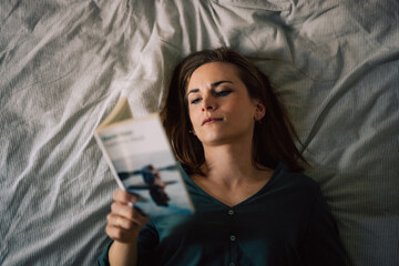 Jeune femme, séduisante en train de lire un livre, couchée sur un lit.