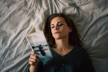 Obraz premium Jeune femme, séduisante en train de lire un livre, couchée sur un lit.