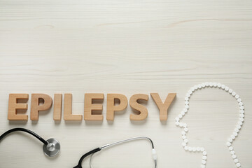 Human head silhouette made of pills, word Epilepsy and stethoscope on white wooden table, flat lay....