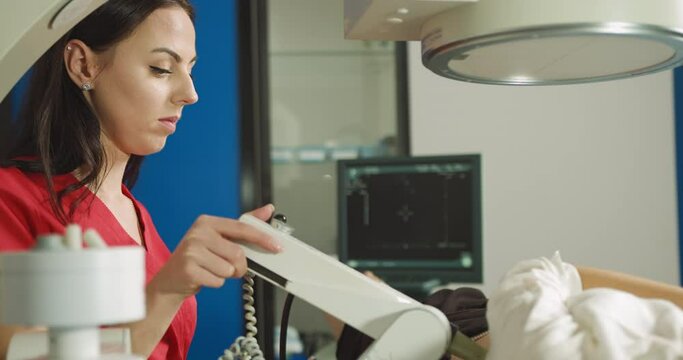 Extracorporeal Shock Wave Therapy. Kidney stone treatment. Side view of woman doctor looking at the digital screen of the lithotriptor to determine kidney stones position. Focus on female doctor