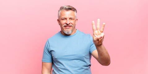 old senior man smiling and looking friendly, showing number three or third with hand forward,...