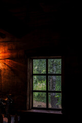 The house is old in the forest. Mysterious mystical fairy light lamp in the scary darkness of the room and a view through the window on a green birch forest