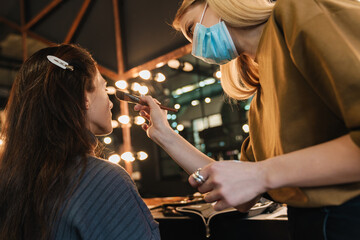 Young blonde woman in face mask working with client in beauty salon