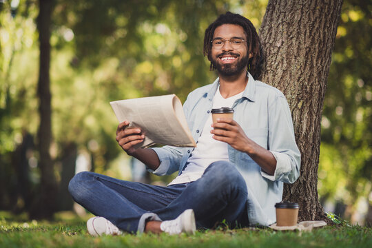 Photo portrait of man in glasses smiling sitting in green park under tree drinking cofee reading newspaper