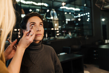 Blonde woman doing makeup for her client in beauty salon
