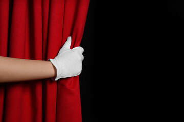 Woman opening red front curtains on black background, closeup. Space for text