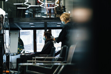 Young woman in face mask dying her client's hair in beauty salon