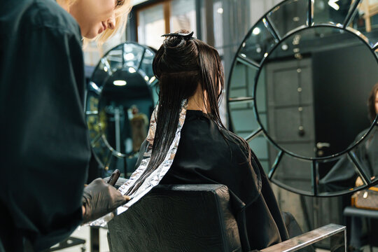 Young blonde woman dying her client's hair in beauty salon
