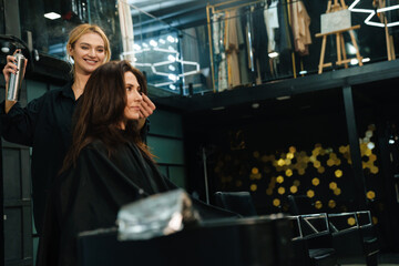 Fototapeta na wymiar Young smiling woman doing hairstyle for her client in beauty salon