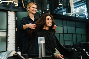 Young smiling woman doing hairstyle for her client in beauty salon