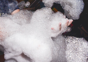 Lots of soap suds in the hands of a man at a foam party in a nightclub background