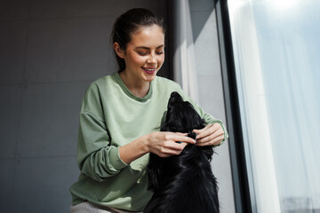 Happy young brunette woman putting collar on her dog