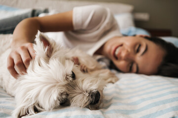 Happy white woman stroking her dog while lying on bed at home