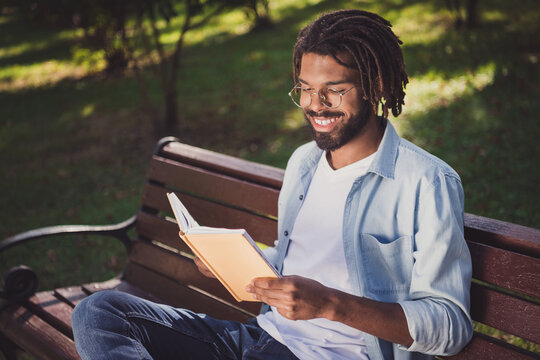 Photo portrait of man in glasses smiling sitting on bench in park reading book spending free time