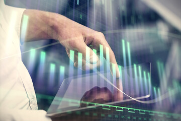 Double exposure of man's hands holding and using a digital device and forex graph drawing. Financial market concept.