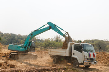 Obraz premium Excavator digging the soil into a truck ,In the construction site area outdoor