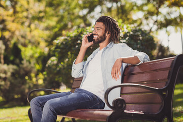 Profile side view portrait of attractive cheerful guy traveler sitting on bench calling friend talking urban sunny day outside outdoor