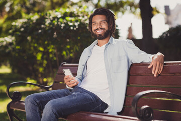 Obraz premium Portrait of attractive cheerful guy sitting on bench using gadget spending free time urban sunny day outside outdoor