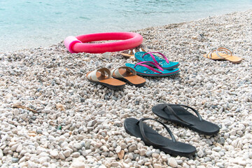 Beach scene. Pairs of flip flop sandals lying on on sea pebble beach