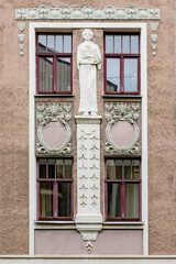 Detail of brown pink grey Art Nouveau building facade of four windows with dark red frames and decoration at renovation needed building in Riga, Latvia, Europe