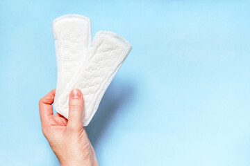 Panty Liner In Hand. Girl's Hand Holding Two Clean Sanitary Daily Pads On Blue Background. Intimate Product. Female Hygiene Concept