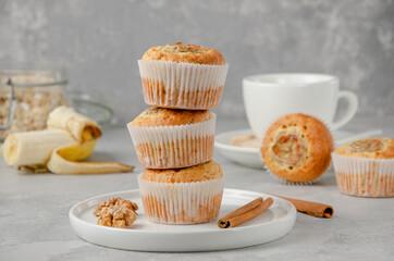 Stack of Banana muffins with oatmeal, walnuts and cinnamon on a white plate on gray concrete background. Healthy dessert.