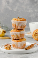 Stack of Banana muffins with oatmeal, walnuts and cinnamon on a white plate on gray concrete background. Healthy dessert. Copy space.
