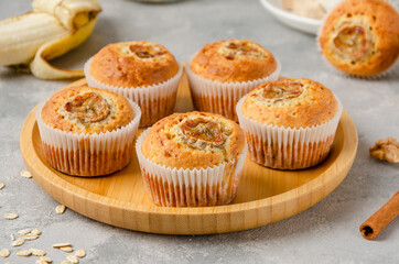 Banana muffins with oatmeal, walnuts and cinnamon on a wooden plate on gray concrete background. Healthy dessert.
