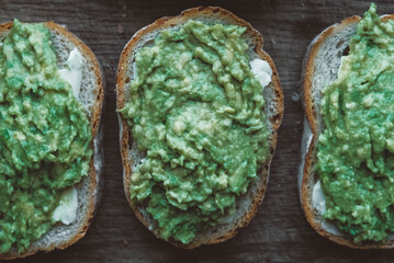 Slices of rye bread with avocado on a wooden background, simple rustic sandwich. Top view. Copy, empty space for text