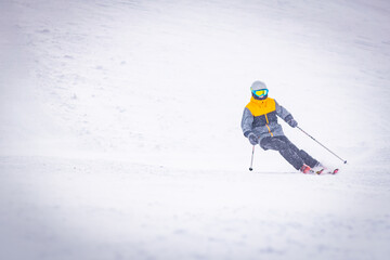 Low angle front view Male person alone skiing downhill in white snowy background. Bad visibility and solo adventure in mountains