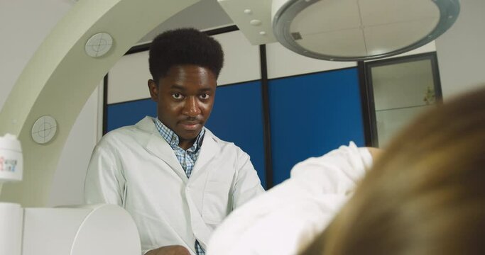 Treatment of urethral stones by non-invasive extracorporeal shock wave lithotripsy. Black man doctor working with modern lithotripter to crush kidney stones for his female patient in modern clinic