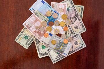 Euros and US Dollars scattered in a pile on a wooden table