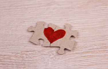 Two pieces of a puzzle with a drawn red heart on a wooden background. Two halves of the heart on puzzles. Love concept