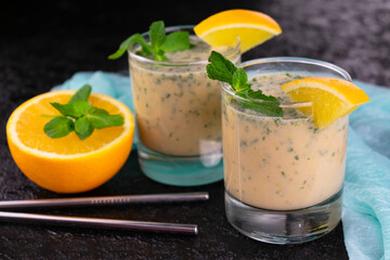 Two glasses of smoothies with mint and orange on a black background.	