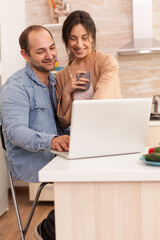 Happy entrepreneur couple working on laptop in kitchen during morning. Happy loving cheerful romantic in love couple at home using modern wifi wireless internet technology