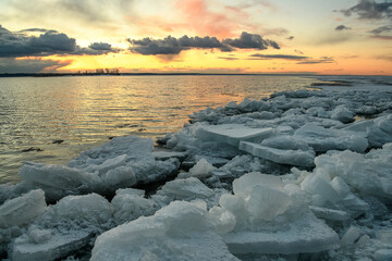 Beautiful sunset over the snowy sea on a frosty weather. Icy boulders along the shore.