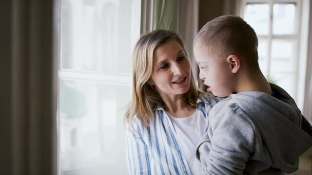 Single mother with down syndrome child at home, talking by window.